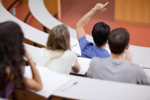Image d'un étudiant levant la main pendant un cours en amphithéâtre. Soutien scolaire pour les étudiants du supérieur Vend'études.